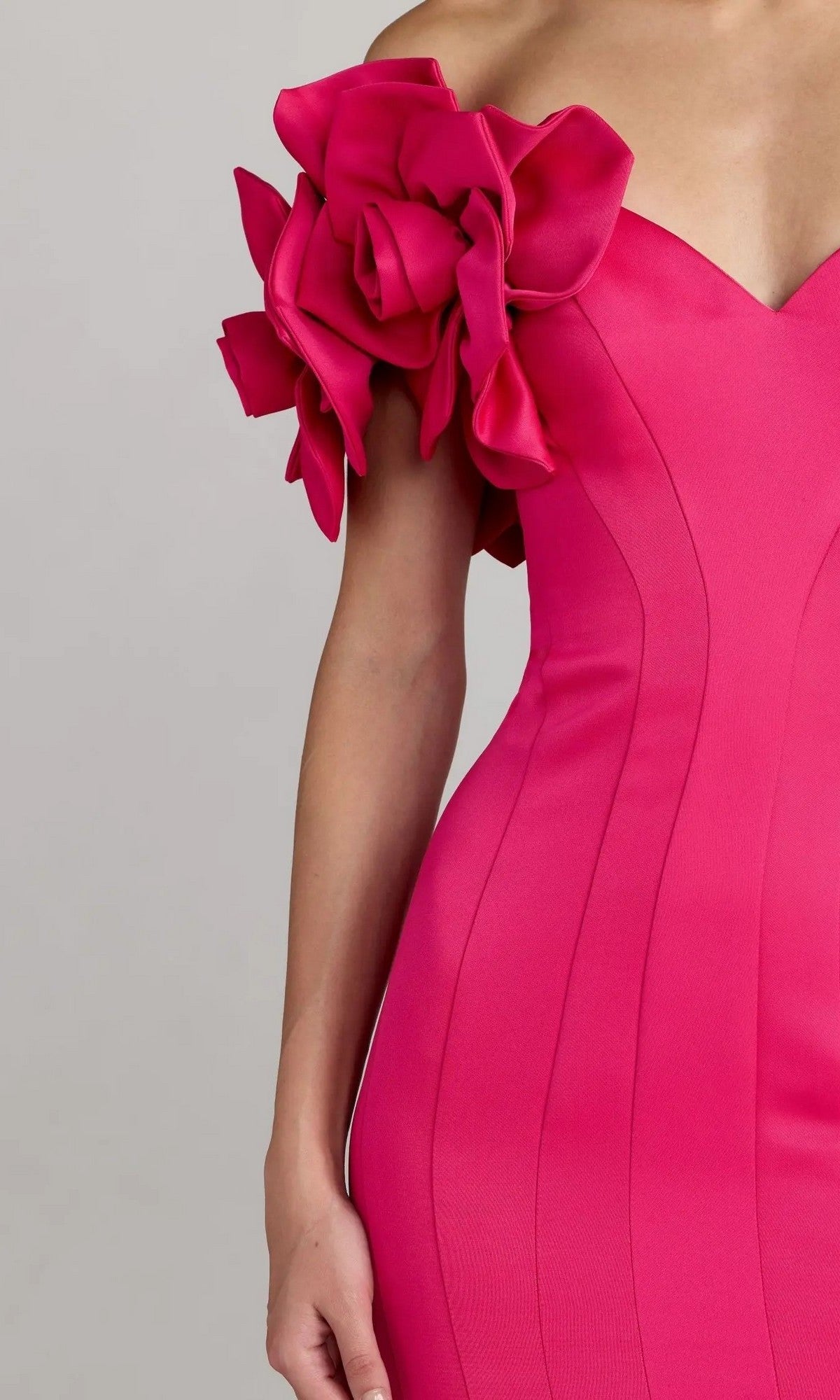 A person wearing the Mac Duggal 21263 Long Formal Dress—a fitted, vibrant pink gown featuring a dramatic, ruffled floral detail on one shoulder—shown from the upper chest to the hip.