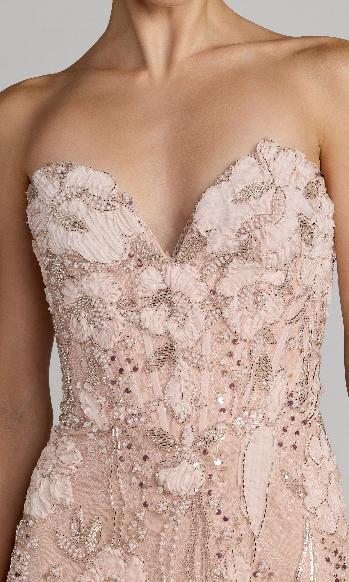 A person shown from chest to waist wearing the Mac Duggal 21283 long formal dress, a strapless blush pink gown featuring a corset bodice adorned with floral embroidery, sequins, beading, and delicate floral appliques.