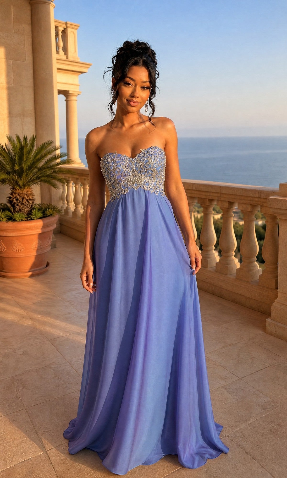 Woman in a La Femme Embroidered Chiffon Prom Dress 21289, strapless, floor-length, and blue violet with gold embroidery, stands on a stone balcony overlooking the ocean.