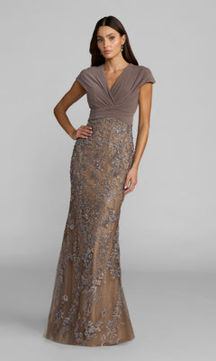 A woman wearing the Mac Duggal 21291 long formal dress in Taupe Multi, featuring cap sleeves, a fitted bodice, and floral embroidery on a sheer, floor-length skirt, stands against a plain gray background.