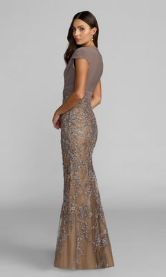 A woman models the Mac Duggal 21291 long formal dress—featuring a fitted, short-sleeve taupe top and a floor-length sheer skirt adorned with intricate silver floral embroidery—against a plain backdrop, embodying the elegance of haute couture.