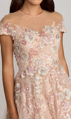 A woman wearing the Mac Duggal 21296 tea-length party dress, which features a sheer short-sleeved bodice embellished with pink and blue floral embroidery and sparkling sequin details, complemented by an elegant A-line tulle skirt.