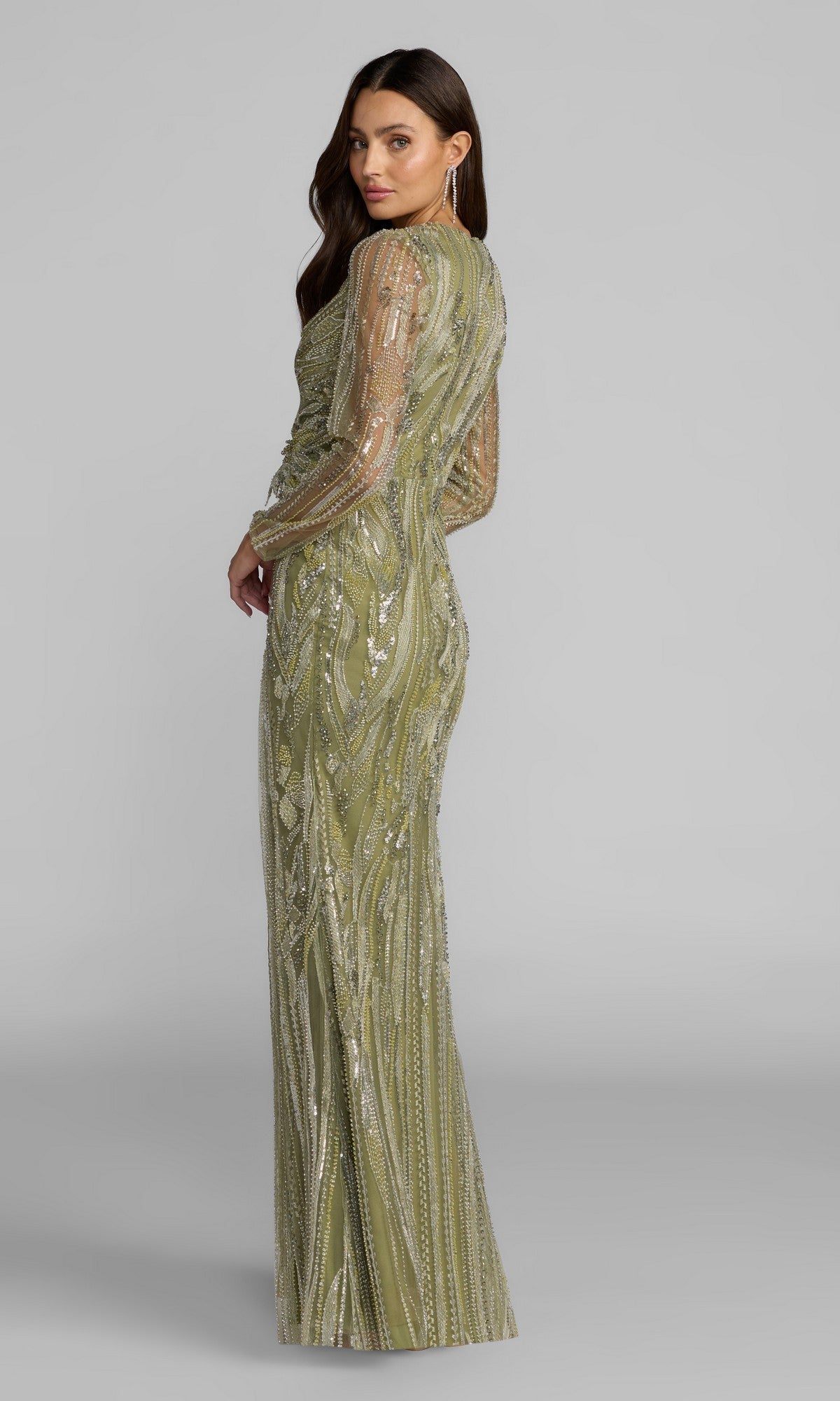 Wearing the Long Formal Dress: Mac Duggal 21306, a woman faces away in a floor-length, olive green evening gown featuring sheer beaded long sleeves and intricate hand-embellished sequin detailing in the collection’s signature style, set against a plain gray backdrop.