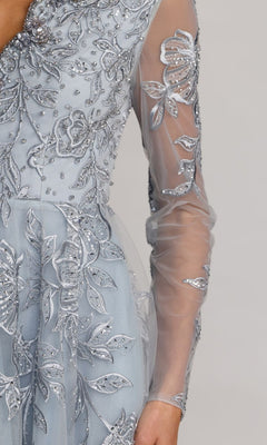 A close-up of the Mac Duggal 21307 long formal dress, featuring sheer long sleeves, silver floral-beaded embroidery, and intricate beadwork, shown on a person against a plain background.