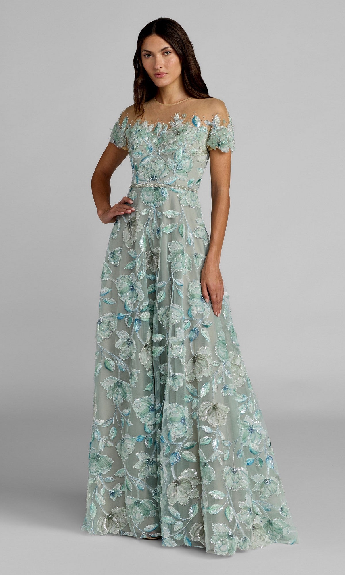 A woman model wears the Mac Duggal 21339 long formal dress in Sage Multi, featuring off-the-shoulder styling and floor-length beaded floral embroidery, posed against a plain gray background.