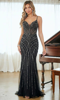 A woman stands indoors in front of a piano, wearing the Tight Long Beaded Prom Dress: Amelia Couture 2135—a sleeveless black gown with silver geometric beading and a floor-length sheer overlay.