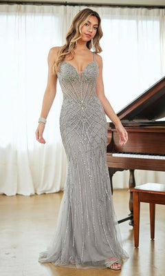 A woman stands indoors in front of a piano, wearing the Amelia Couture 2135— a tight long beaded prom dress with spaghetti straps and transparent panels.
