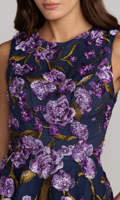 Wearing the Ankle-Length Party Dress: Mac Duggal 21358, a woman showcases an elegant sleeveless navy blue party dress, featuring intricate purple floral embroidery and gold branches on the bodice, complemented by a flowing tulle A-line skirt.