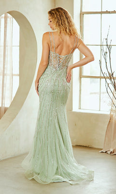 A woman with wavy blonde hair wears the Amelia Couture 2136-2134 Lace-Up Beaded Prom Gown, a light green dress with sequin embellishments, an open back, and corset bodice, standing indoors by large windows.