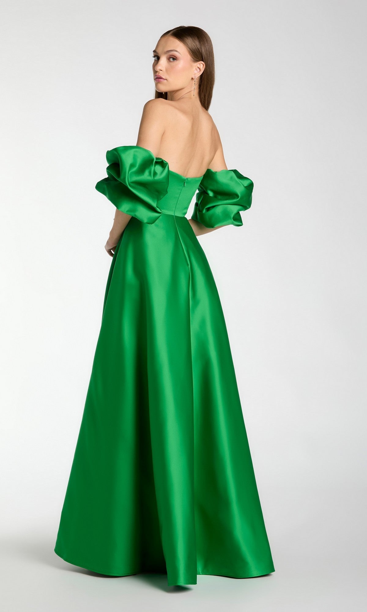 A woman is wearing the Mac Duggal 21375 long formal dress, a strapless, floor-length green satin ballgown featuring voluminous off-the-shoulder puff sleeves, standing against a plain light background.