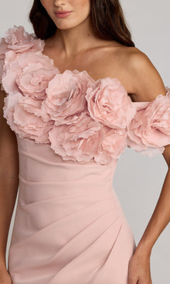 A woman wears the Mac Duggal 21383 long formal dress in light pink, featuring an off-shoulder design adorned with large, layered 3D floral appliqué details across the neckline and upper bodice.