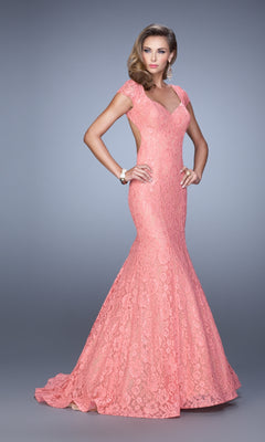 A woman models the coral La Femme 21509, a cap-sleeve long lace prom dress with open back and slight mermaid train, against a plain gray background.