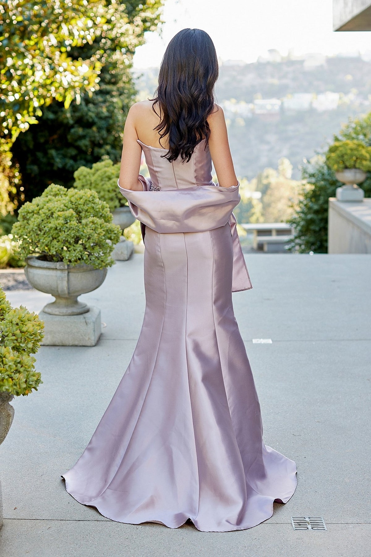 Back view of a woman wearing the Amelia Couture 2162, a beaded, strapless, floor-length lavender evening gown with a matching stole draped around her arms.