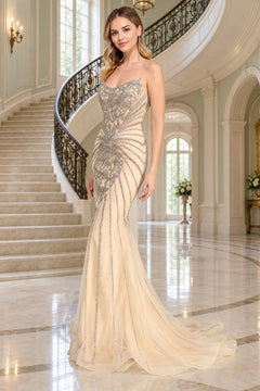 Amelia Couture 2165 strapless champagne-colored mermaid prom dress with an embellished bodice and flared skirt, standing in a grand foyer with a curved staircase.