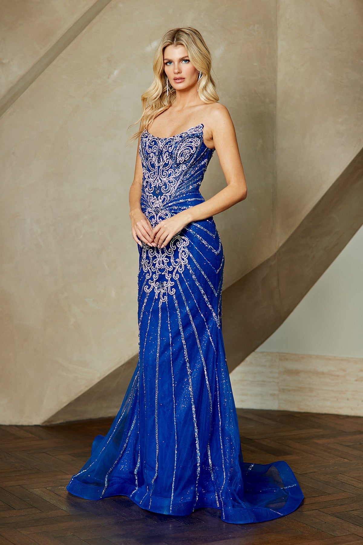 Amelia Couture 2165 floor-length blue mermaid prom dress with silver filigree embroidery, a corset-style bodice, and a flared skirt.