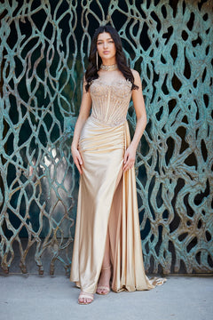 A woman wears a champagne-colored Long Prom Dress: Amelia Couture 2169, featuring a strapless beaded corset bodice and a high leg slit.