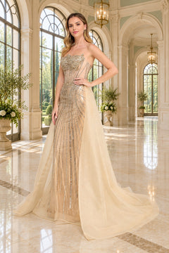 Amelia Couture 2172 strapless champagne prom dress featuring a beaded bodice and a sheer, flowing detachable overskirt.