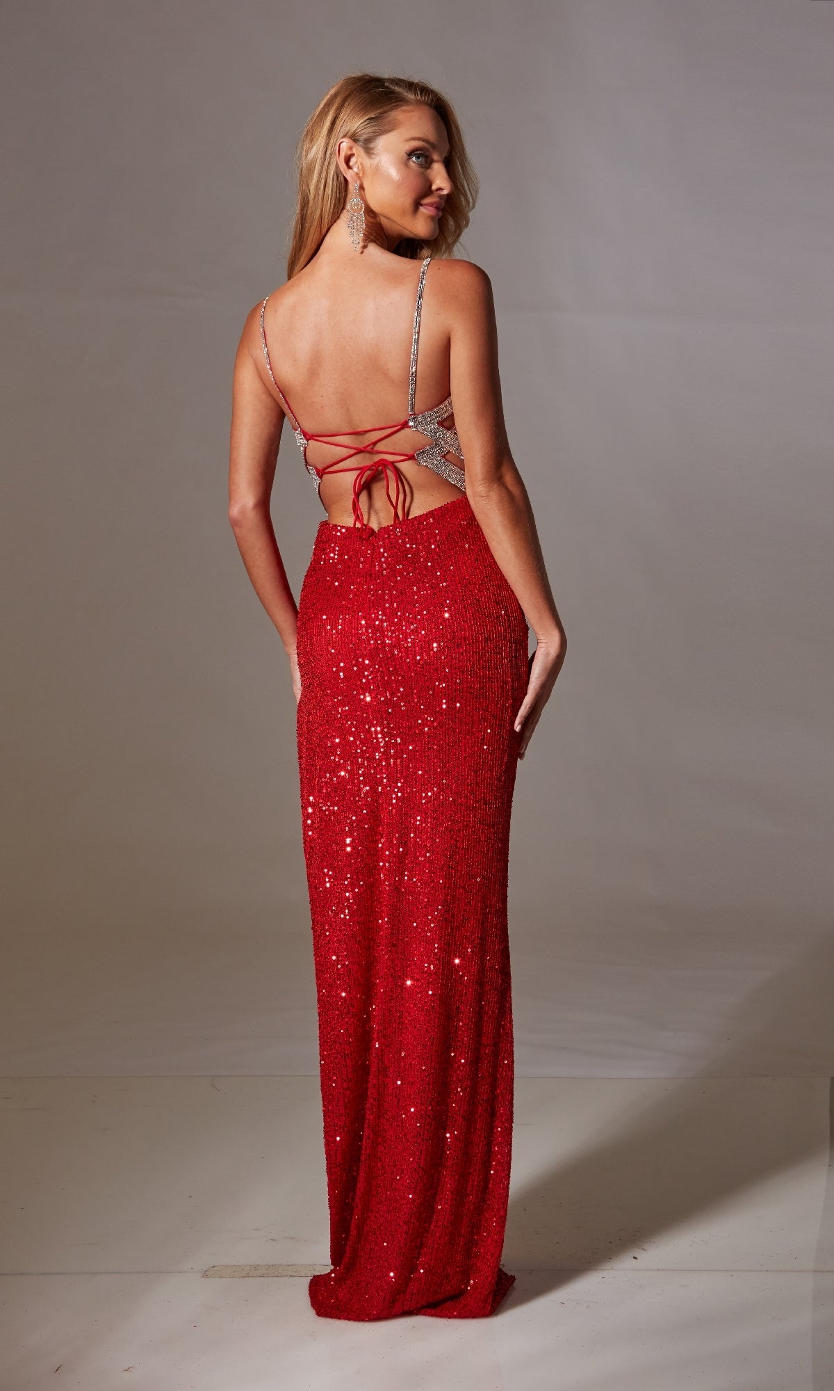 A woman models the Lace-Up Long Sequin Prom Dress: Aerie Couture 218—a red gown with an open back and lace-up straps—standing and glancing over her shoulder.