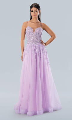 A woman wears the Stella Couture 22027, a long lavender glitter tulle prom dress with thin straps and a beaded fitted bodice, standing against a plain light background.