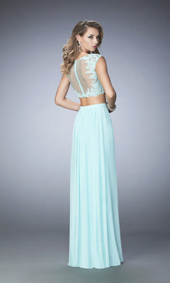A woman models the La Femme Two-Piece Lace-Top Jersey Prom Dress 22110, showing off its light blue hue and sheer-back lace details with her back to the camera against a plain gray background.