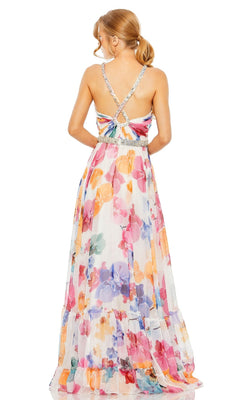 A woman stands facing away, wearing the Long Formal Dress 2219 by Mac Duggal—a sleeveless, floor-length floral A-line gown featuring crisscross straps and a beaded belt.