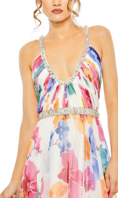 A woman in the Long Formal Dress 2219 by Mac Duggal, featuring an a-line silhouette with colorful floral prints, rhinestone-embellished straps, and a beaded belt, stands against a white background.
