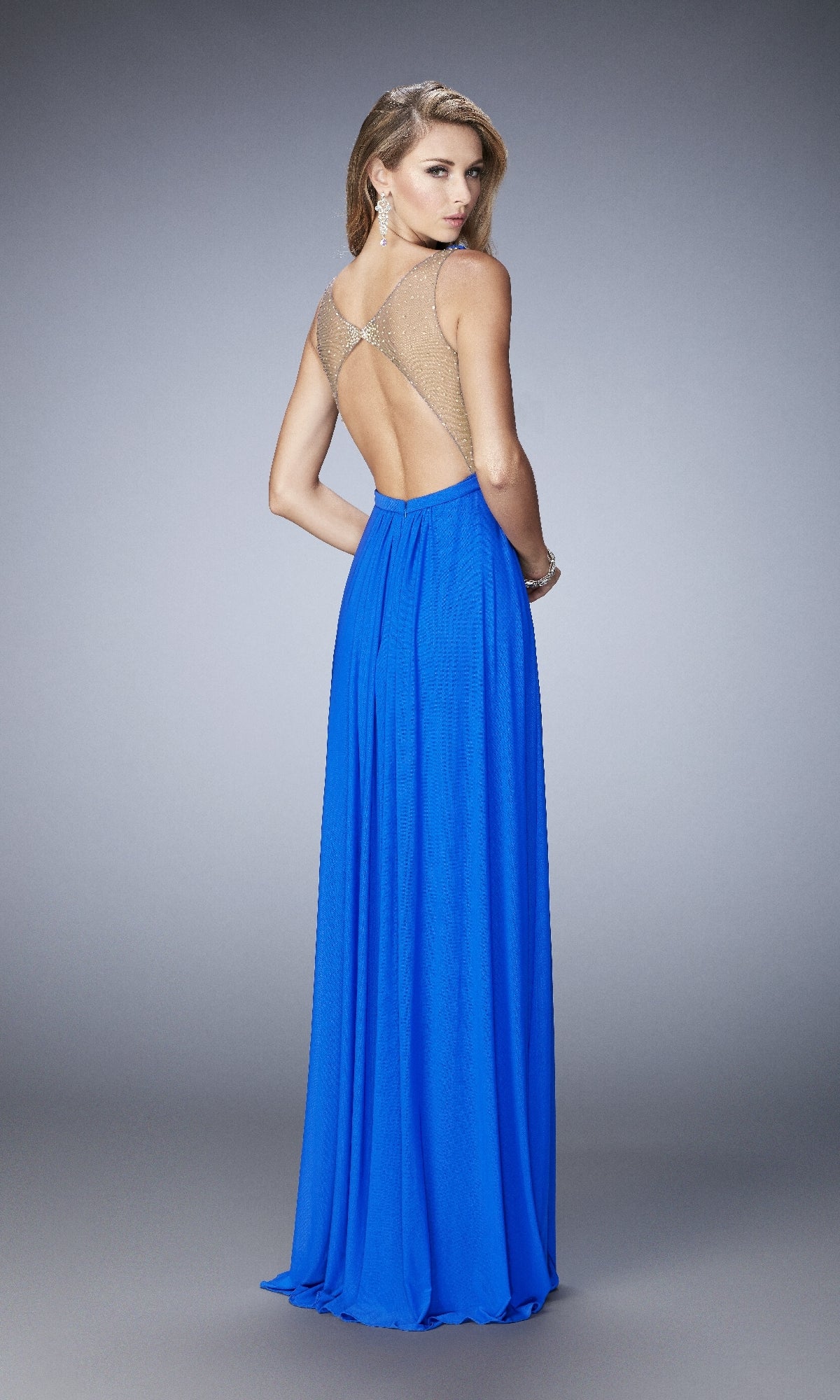 Woman wearing the La Femme 22238 long prom dress in royal blue with sheer straps and open back, standing and looking over her shoulder against a plain gray background.