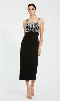 A woman in the Mac Duggal 2226 Black Midi Wedding Guest Dress with silver-embellished bodice stands against a plain white background.