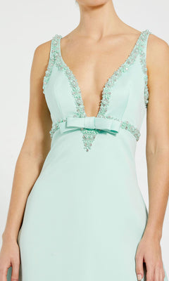 A woman wears the Mint Short Wedding Guest Dress: Mac Duggal 2228, a sleeveless mint dress with a deep V-neckline, beaded embellishments, and a waist bow—ideal for cocktail parties.