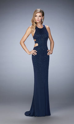 A woman poses in the La Femme 22287 long prom dress, a sleeveless navy blue gown with beads and side cutouts, against a plain gray background.