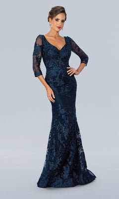 A woman models the Stella Couture 22361 long formal dress in navy, featuring a v-neckline, three-quarter sheer sleeves, and intricate lace embroidery, standing before a plain light gray background.
