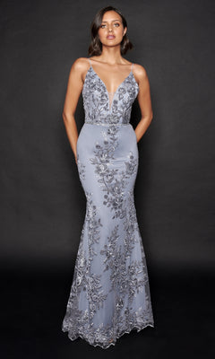 A woman poses against a black background wearing the Nina Canacci 2240, a floor-length, fitted silver-gray formal dress with floral embroidery, thin straps, and a subtle mermaid silhouette.