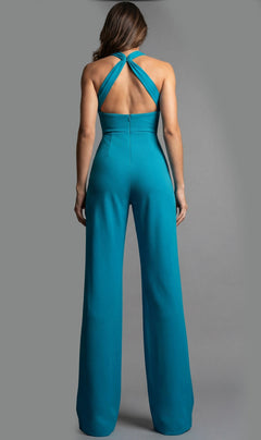 A woman stands with her back to the camera, modeling the Jovani 22542 long jumpsuit in teal. This formal, sleeveless jumpsuit features a crisscross halter neckline and a wide-leg silhouette, set against a plain gray background.