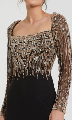 A woman wears the Mac Duggal 2256 Long Sleeve Long Formal Dress, featuring sheer sleeves and intricate gold and silver bead embellishments on the bodice and arms.