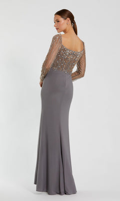 A woman models the Mac Duggal 2256 long sleeve formal dress, featuring a fitted gray silhouette with sheer beaded sleeves and a scoop back, posed against a plain white background.