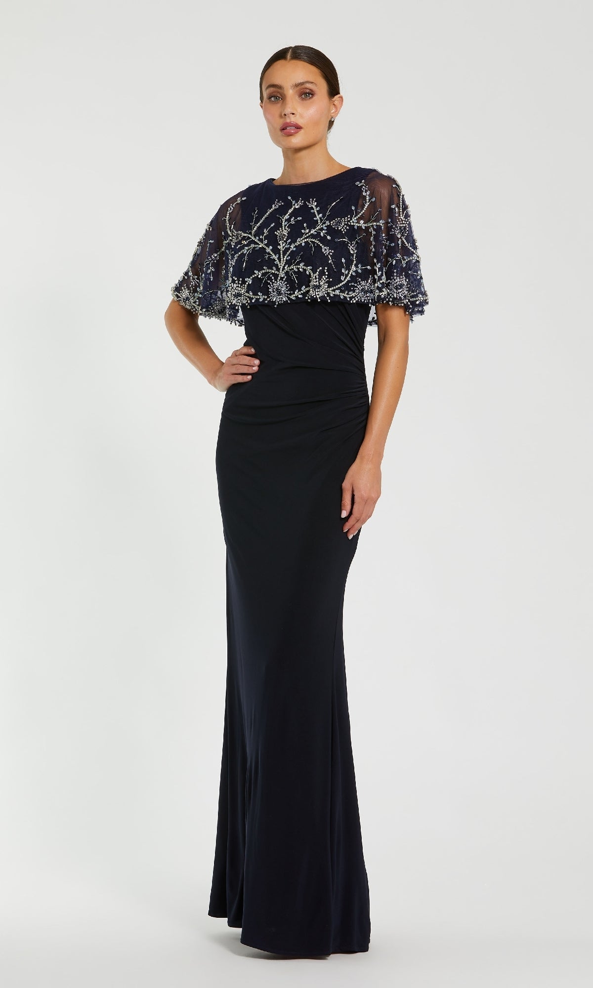 Woman wearing a dark navy blue evening gown with silver embellishments on a white background