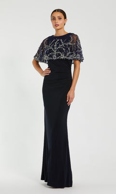 Woman wearing a dark navy blue evening gown with silver embellishments on a white background