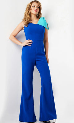 A woman stands against a plain white background, wearing the Jovani 22589 long jumpsuit in royal and turquoise—a stylish sleeveless wide-leg design with a light blue bow accenting one shoulder.
