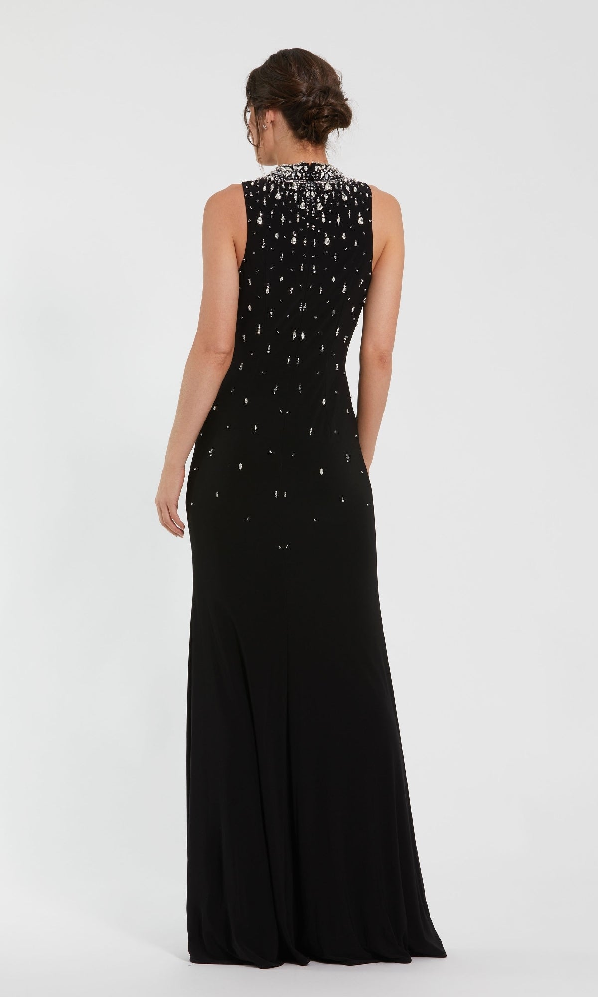 A woman stands with her back to the camera against a white background, wearing the Mac Duggal 2260 high-neck long black formal gown featuring a sleeveless design, floor-length cut, and white embellished beading on the upper back.