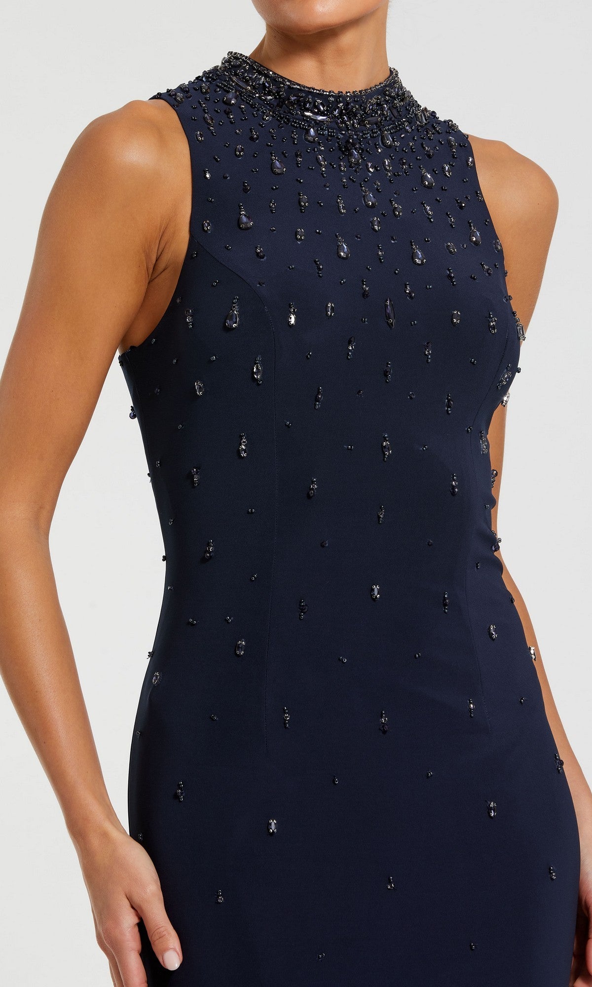 A woman wears the Mac Duggal 2260 high-neck long black formal gown, sleeveless with bead embellishments, her hand resting by her side.