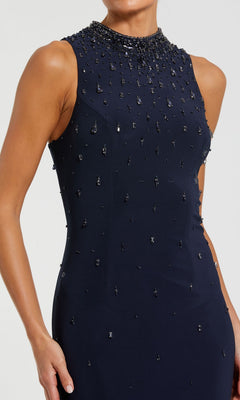 A woman wears the Mac Duggal 2260 high-neck long black formal gown, sleeveless with bead embellishments, her hand resting by her side.