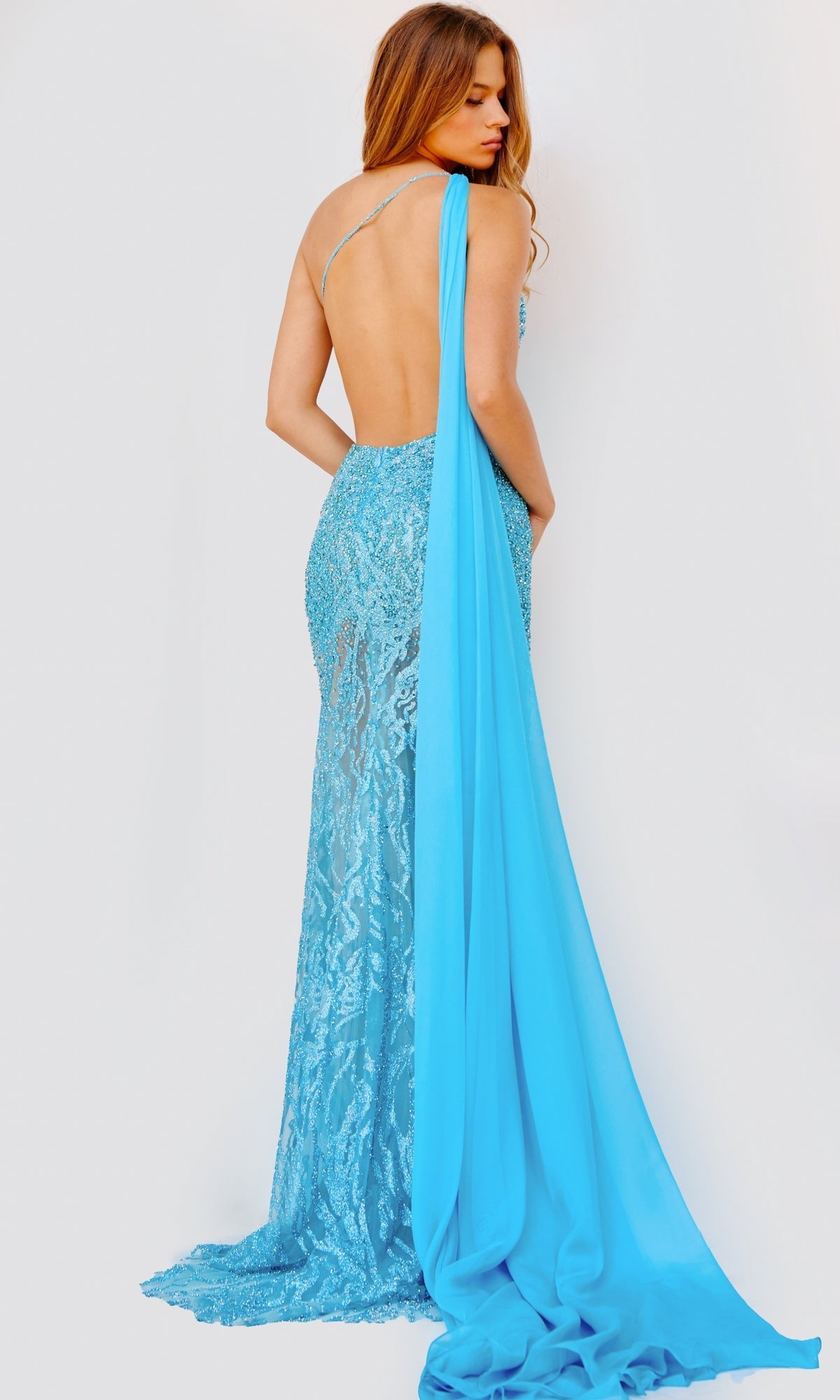 A woman wears the Jovani Shoulder-Drape Sheer Long Prom Dress 22602, a backless, floor-length sequin-print gown with a long blue drape, standing against a plain light background.