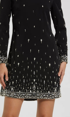 Someone wears the Mac Duggal 2262 short semi-formal dress, a black crepe shift with long sleeves, featuring clustered silver crystal beading on the cuffs and hem.
