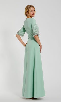Woman posing in the Mac Duggal 2270 Short Sleeve Sleek Formal Dress, featuring light green fabric and embellished sleeves, standing slightly turned against a plain background.