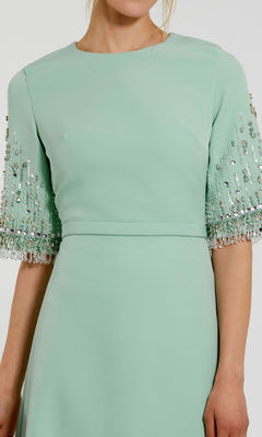 A woman wearing the Mac Duggal 2270 Short Sleeve Sleek Formal Dress in mint green, featuring beaded embellishments on the sleeves, shown from shoulders to knees.