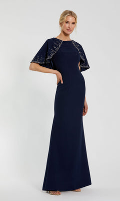 A woman poses in the Mac Duggal 2271 Caped Long Blue Formal Dress—floor-length, fitted, with beaded cape sleeves—an elegant mother of the bride choice, set against a plain light background.
