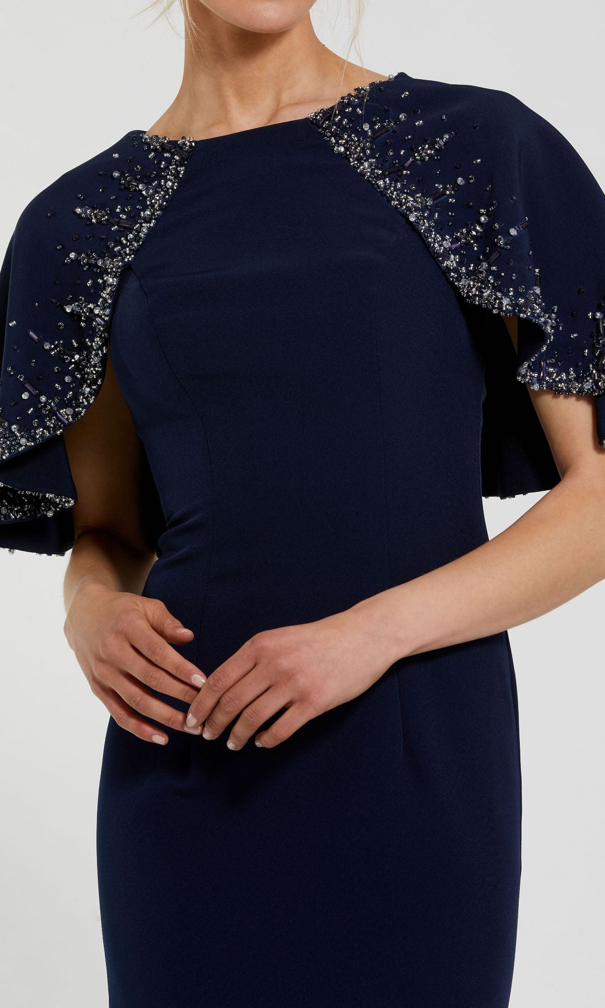 A mother of the bride stands gracefully in the Mac Duggal 2271 Caped Long Blue Formal Dress, featuring beaded embellishments on short cape sleeves, with her hands clasped at her waist.