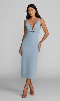 A woman stands against a plain background in the Mac Duggal 2276 V-Neck Midi Wedding Guest Dress—sleeveless, light blue, bead-trimmed, deep V-neck—paired with silver high-heeled sandals. Perfect for any semi-formal occasion.