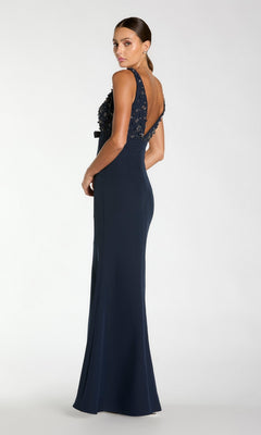 A woman wears the Beaded-Bodice Long Prom Dress by Mac Duggal 2278, featuring a floor-length navy skirt, beaded bodice, and open back as she stands facing away, looking over her shoulder.