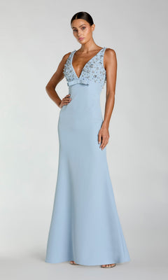 A woman models the Mac Duggal 2278 Beaded-Bodice Long Prom Dress, a sleeveless, floor-length light blue gown with a deep V-neckline and floral embellished beading, against a plain background.